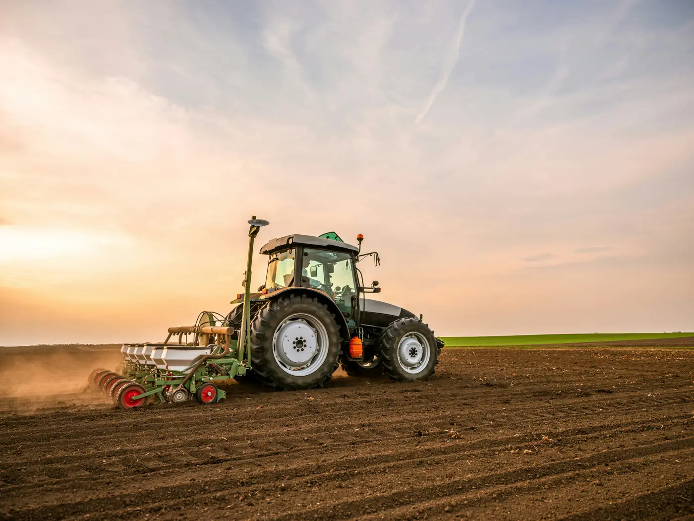 Tracteur et semoir au travail dans un champ, au coucher du soleil
